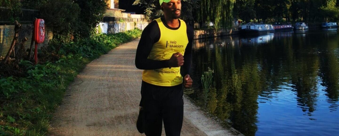 A runner in a Help Musicians vest running next to a canal