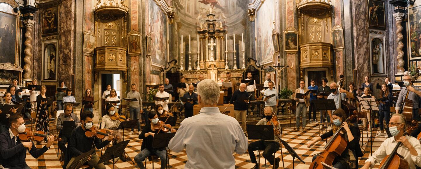 A full orchestra sit in an old chapel being led by a conductor