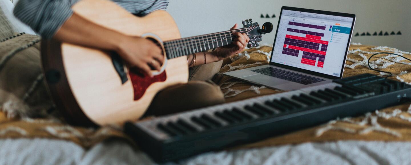 Musician recording themselves playing the keyboard and guitar on their bed